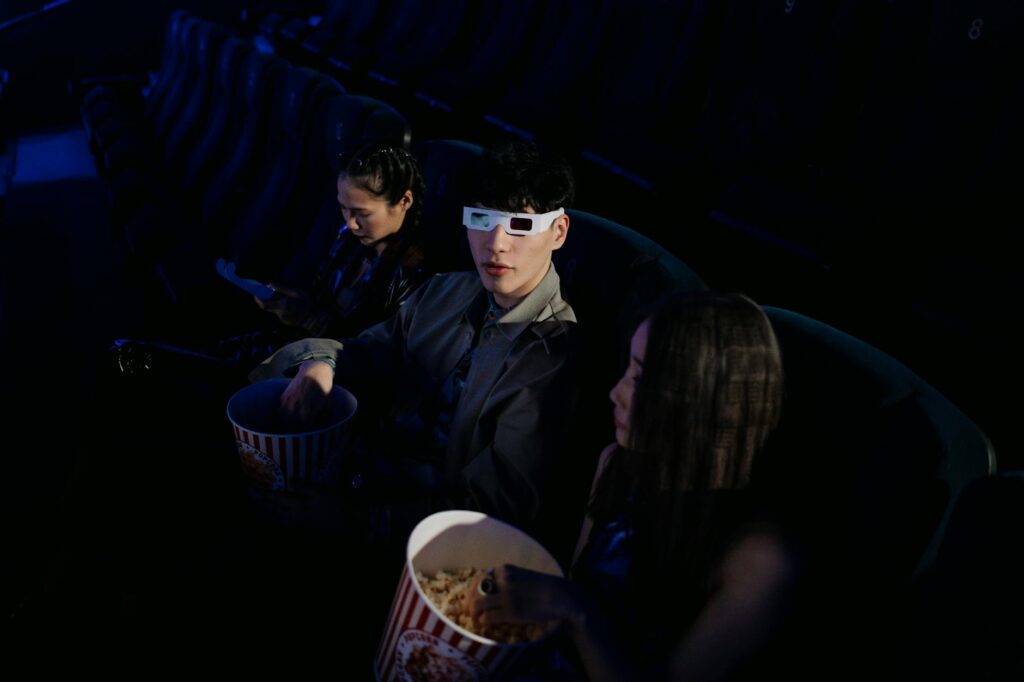 A group of young adults watching a 3D movie at a cinema, enjoying popcorn.