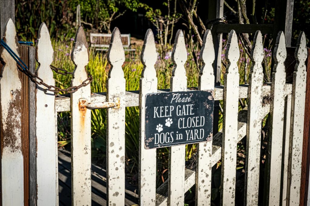 Aged wooden fence with a warning sign to keep gate closed for dog safety.