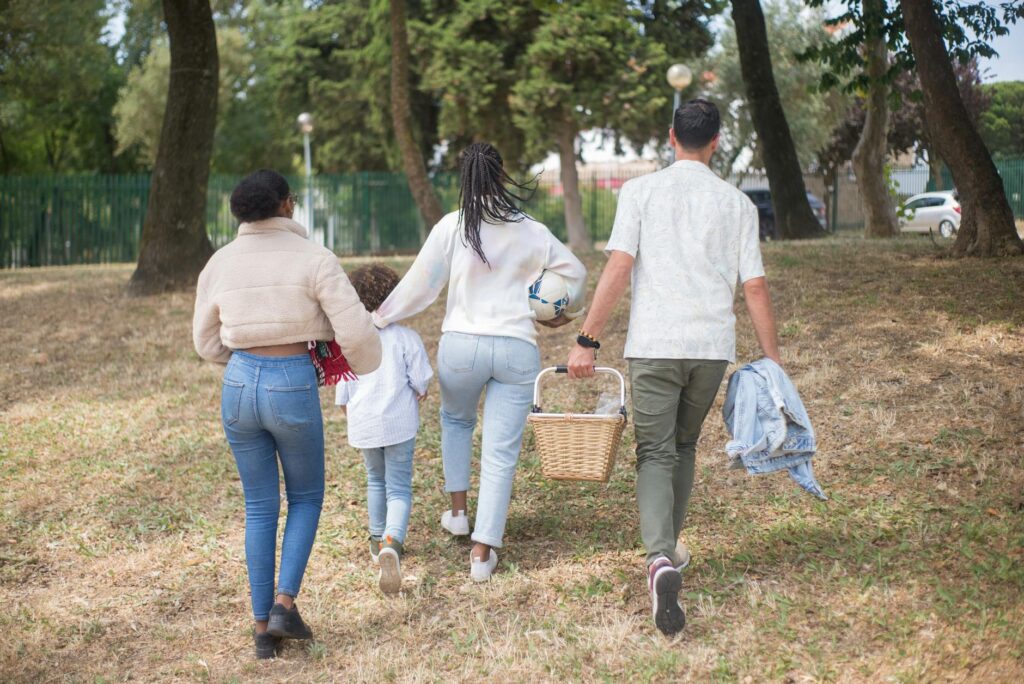 Family walking together carrying picnic basket in a sunny park.