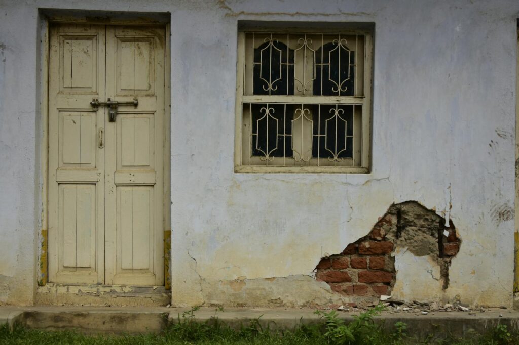 Old building wall with a cracked plaster and barred window, showcasing decay.