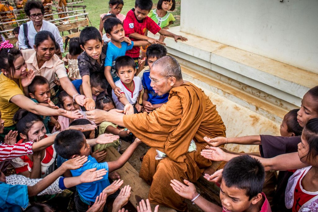 A Buddhist monk sharing gifts with children, capturing a moment of compassion and cultural tradition.