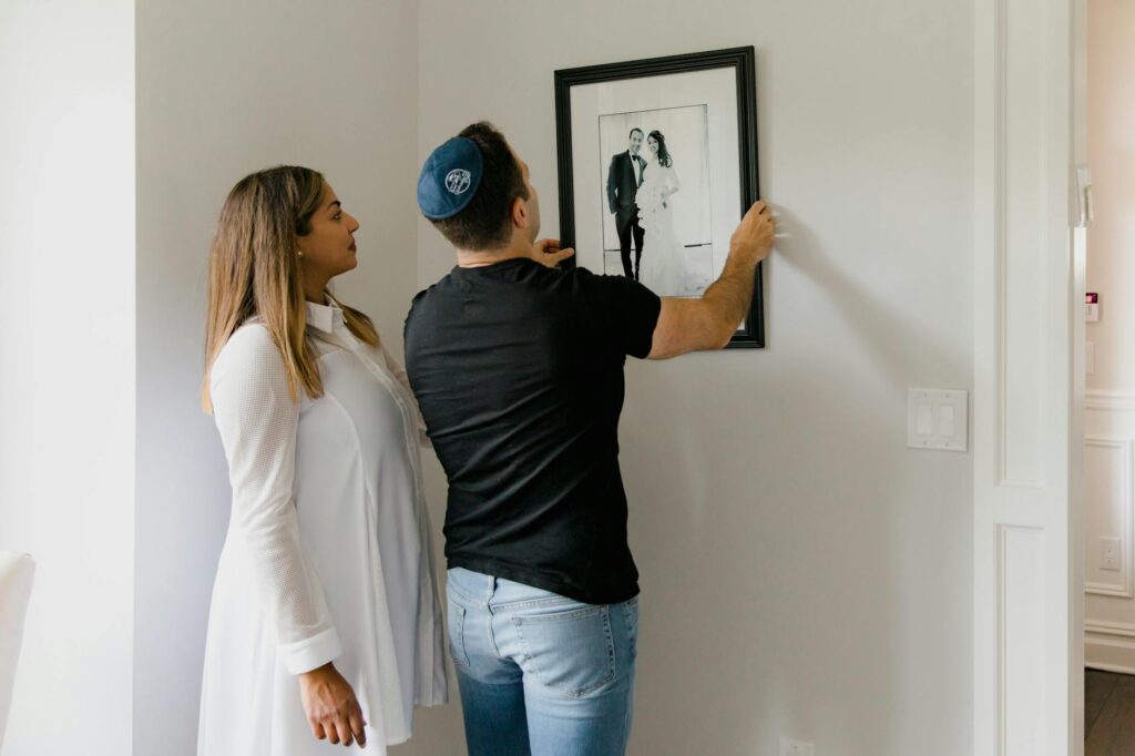 A couple arranges a framed wedding photo on a wall, symbolizing love and togetherness.
