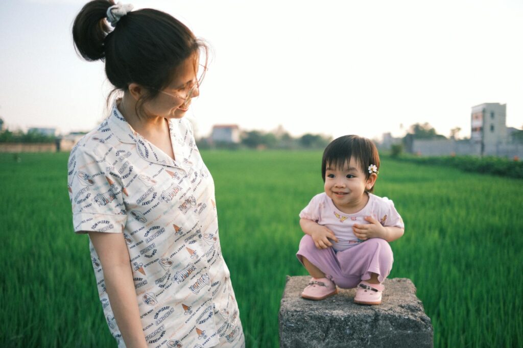 A mother and her child sharing a joyful moment in a lush green field during a sunny day.