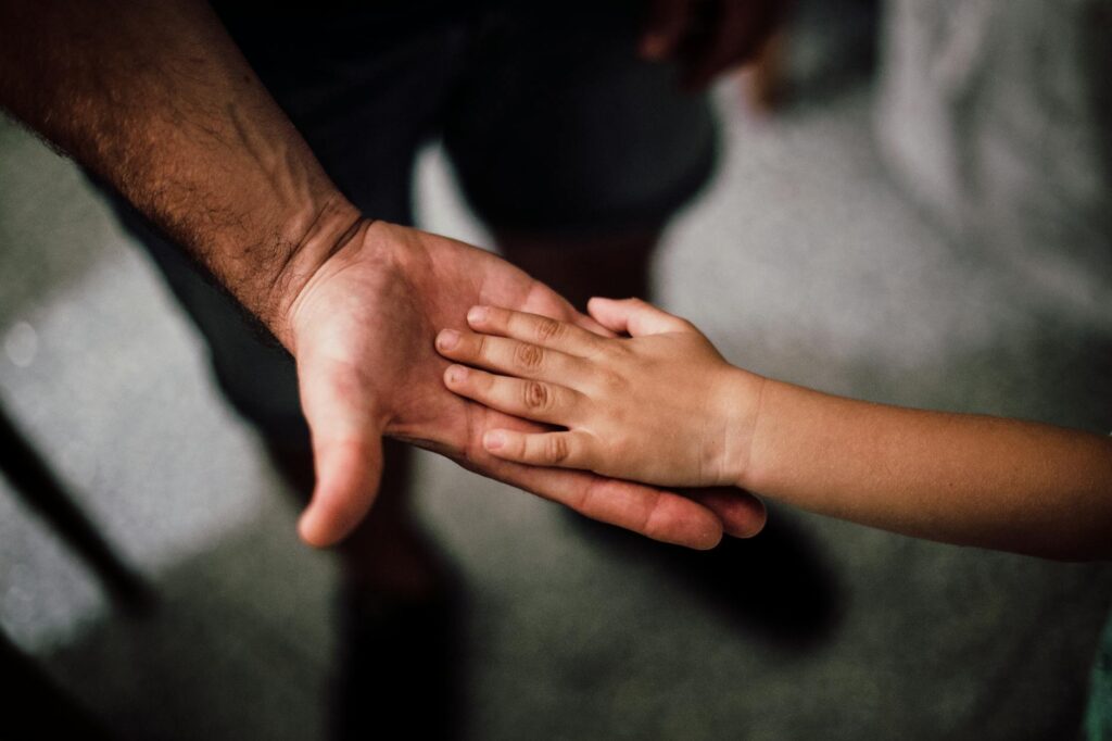 Close-up of a child's hand resting gently on a man's hand, symbolizing love and support.