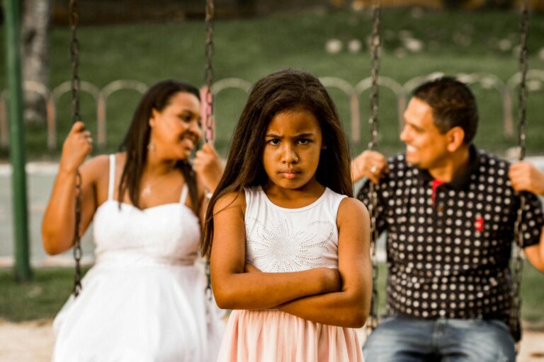A young girl looking grumpy while her parents enjoy swings in a park.