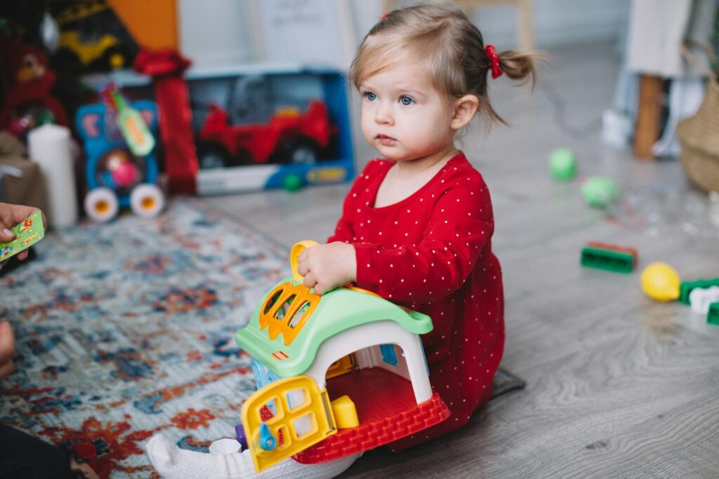 Adorable toddler in red outfit playing with toy house indoors. Perfect for playtime and childhood themes.