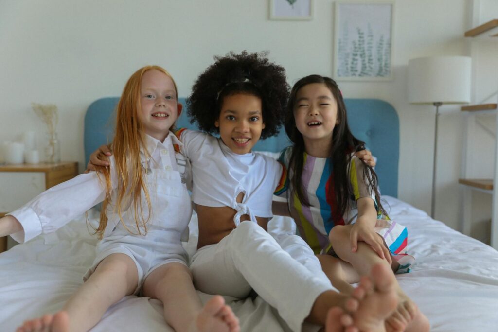 Adorable multiracial little girls embracing and having fun on ved together in modern comfortable room