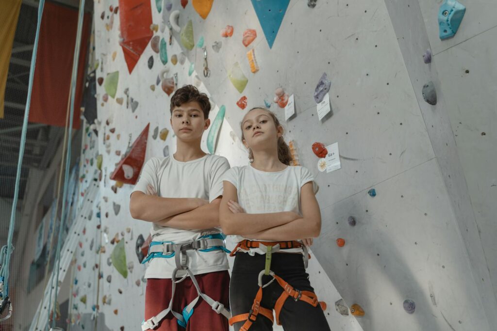 Two youngStrong-willed kids have incredible determination that can become their greatest strength! climbers confidently pose in front of a colorful indoor rock climbing wall.