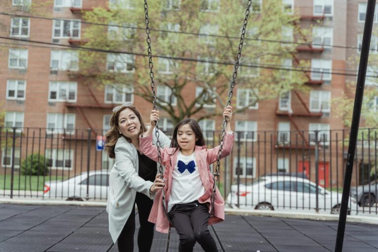 Mother and daughter having fun on a swing set in a city playground.
