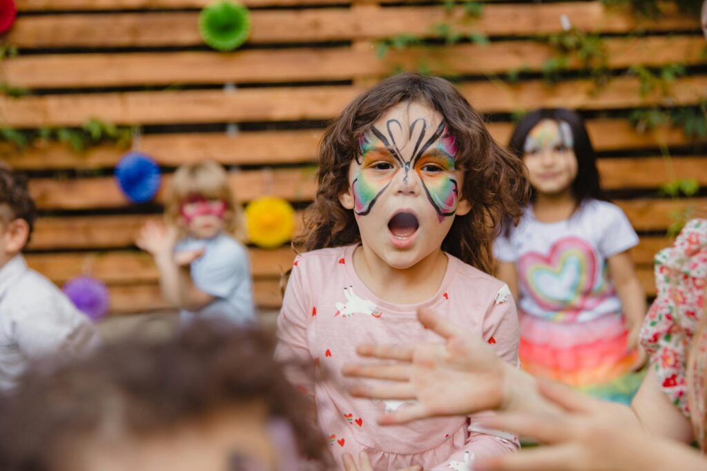 Happy kids enjoying an outdoor party with colorful face paint and playful expressions.