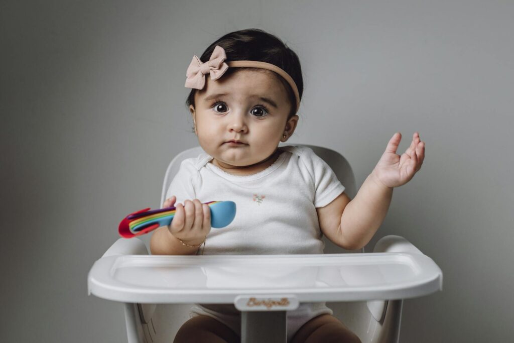 Cute baby girl sitting in a high chair with a colorful toy.