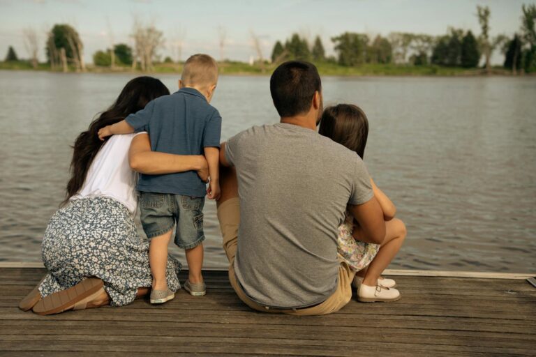 A family of four enjoys a peaceful moment sitting on a wooden deck by the river.