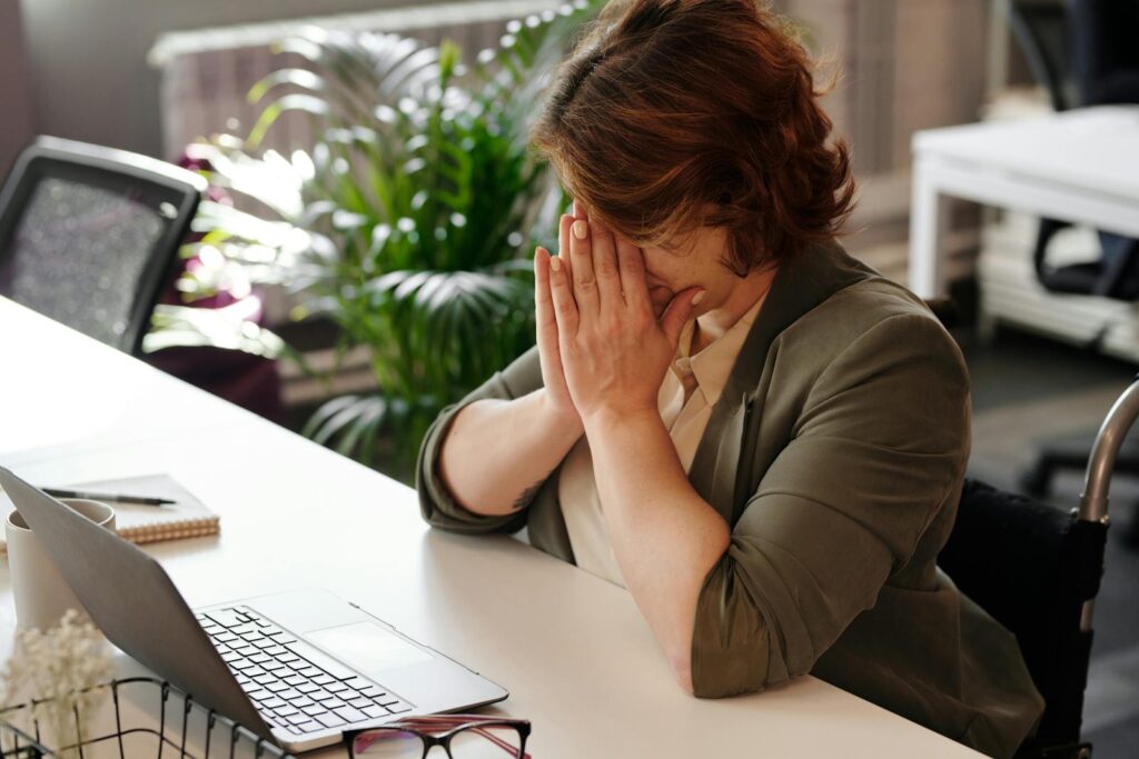 Businesswoman in wheelchair, tired at laptop, symbolizes office stress.