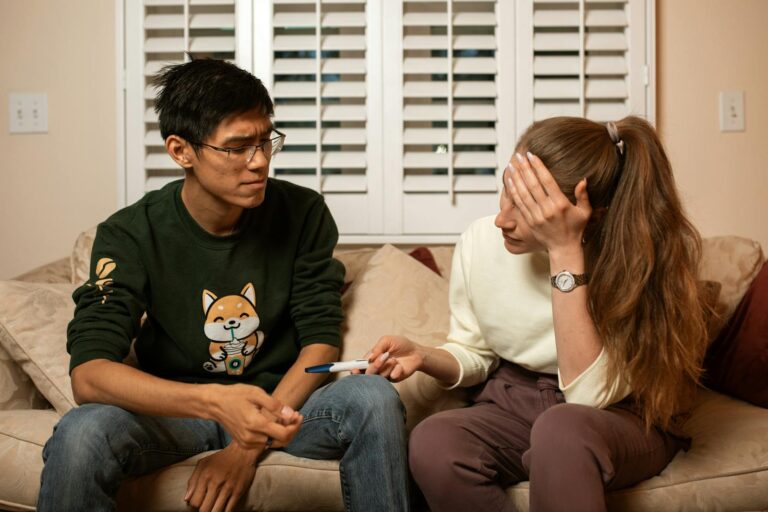 A couple on a couch reacts emotionally to a pregnancy test result, signaling life-changing news.