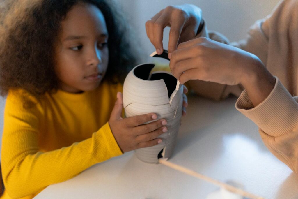 Young siblings carefully fixing a broken vase together at home, fostering creativity and teamwork.
