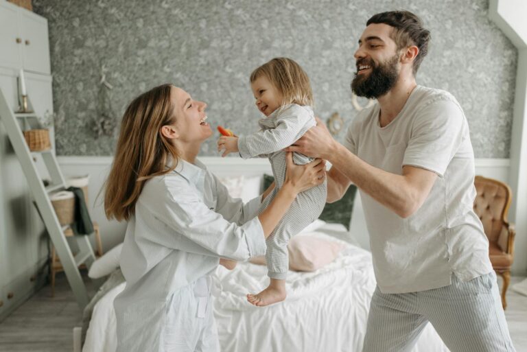 Smiling parents play with their young daughter in a bright, cozy bedroom, creating joyful family memories.