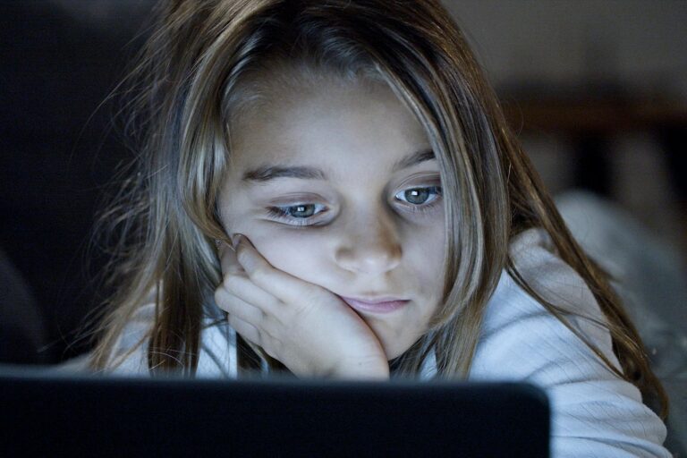 A child is focused on a laptop screen, absorbed in technology during nighttime.