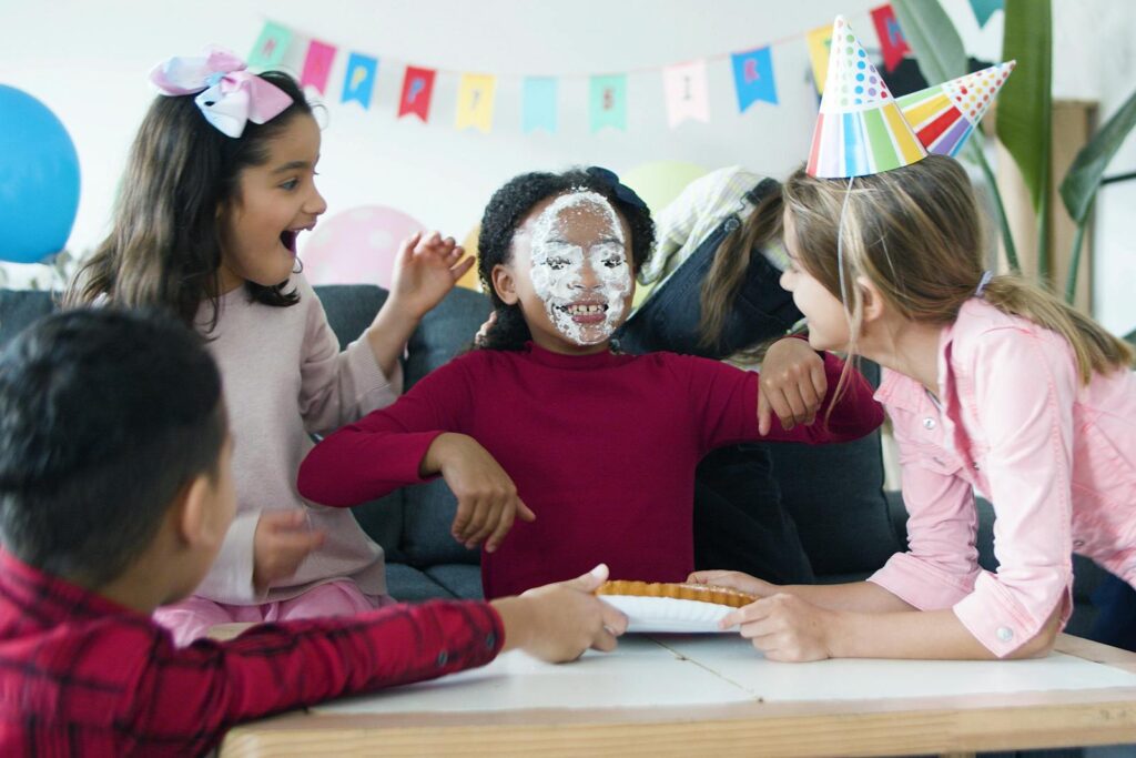 Cheerful kids at a birthday party playing a cake prank with joy and laughter indoors.