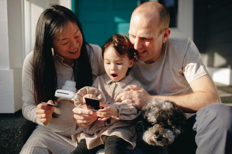 A multicultural family capturing a joyful moment outdoors with their child and pet.