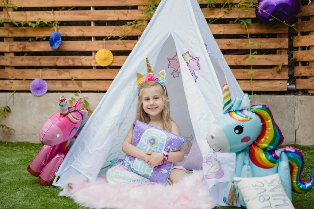 A joyful child in a unicorn-themed setting enjoys a cozy teepee, surrounded by colorful decorations, embodying fun and imagination.
