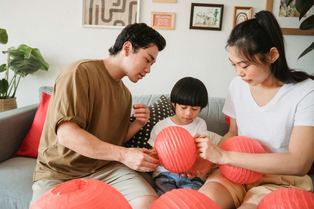 An Asian family sits together indoors, assembling red lanterns and enjoying quality time.