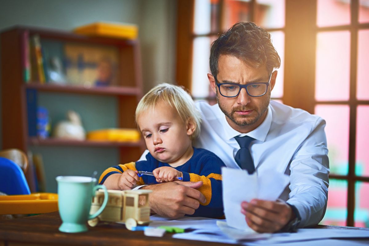 dad with child on lap looking at papers bills stressed