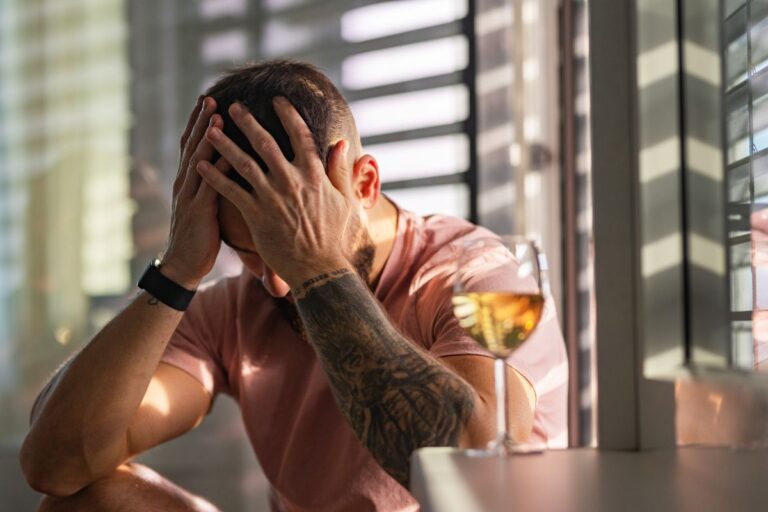 man head in his hands with a wine glass next to him