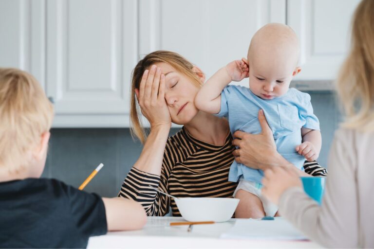 tired mom holding a baby and kids at the table