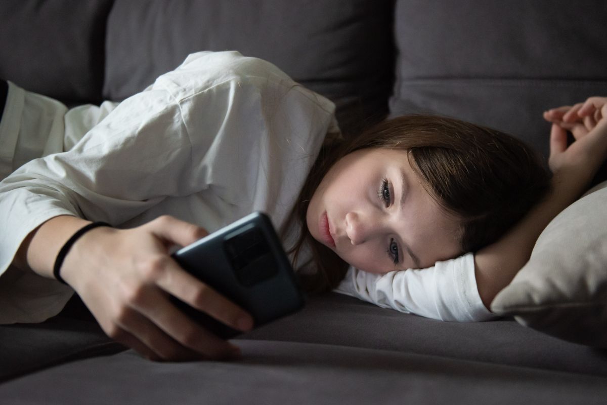 Sad teen on her phone laying on the couch