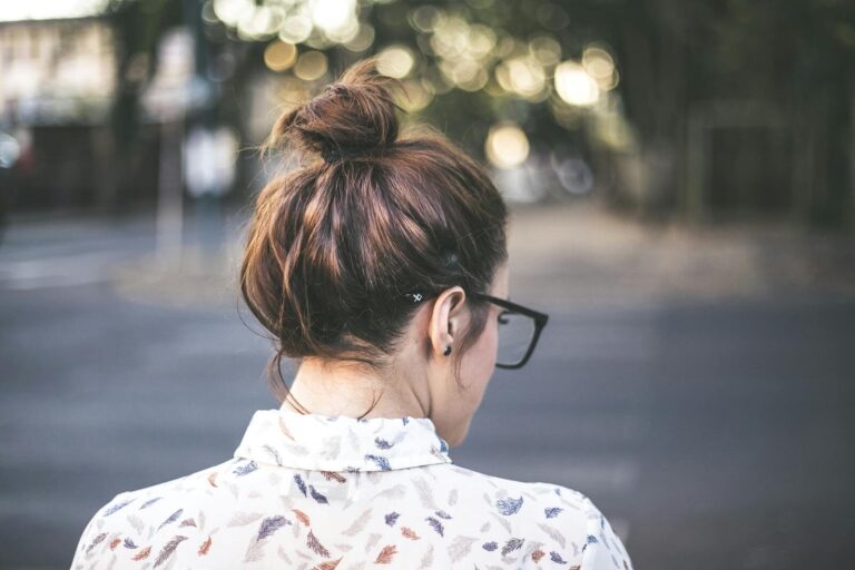 Back view of a woman with glasses and a bun in a natural, blurry background.