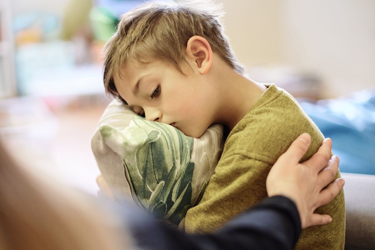 Boy sad hugging a pillow, mom's hand on his back