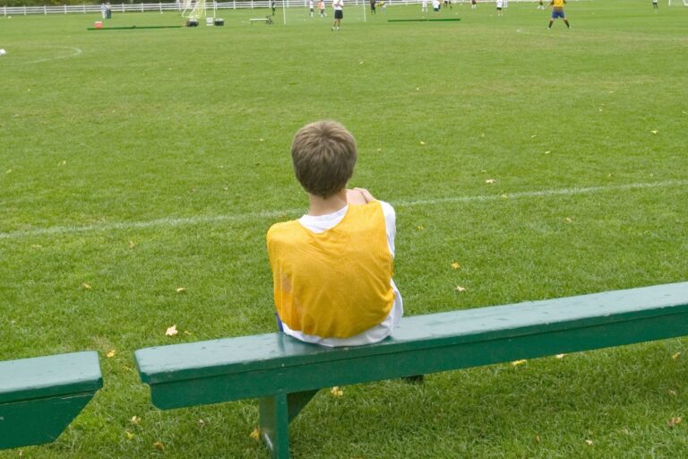 Child sitting on a bench side of the field