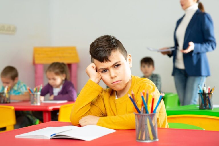 Kid upset at school sitting at his desk looking angry
