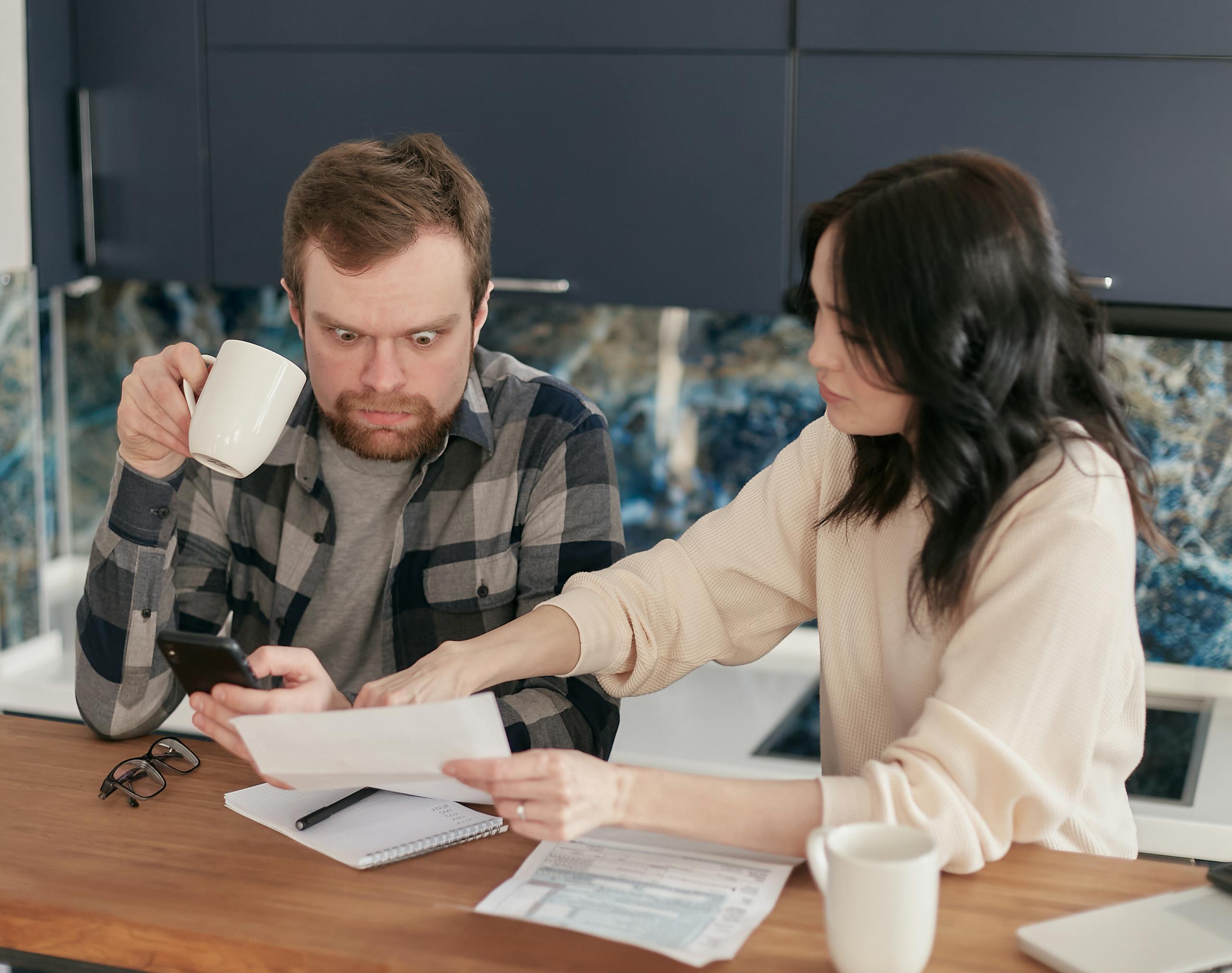 A couple reviews household bills in a kitchen, appearing concerned and focused.