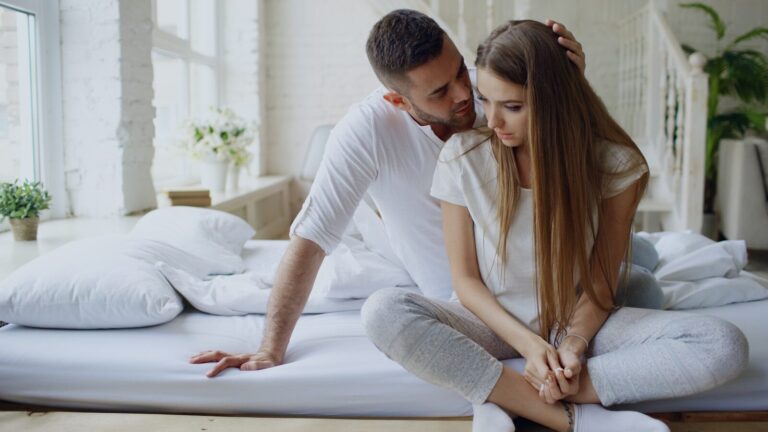 Couple sitting on a bed, man whispers to woman