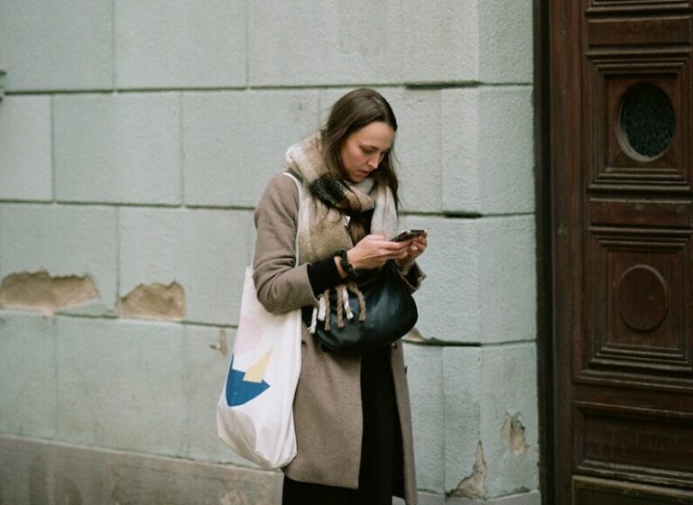 A woman standing on a sidewalk looking at her cell phone
