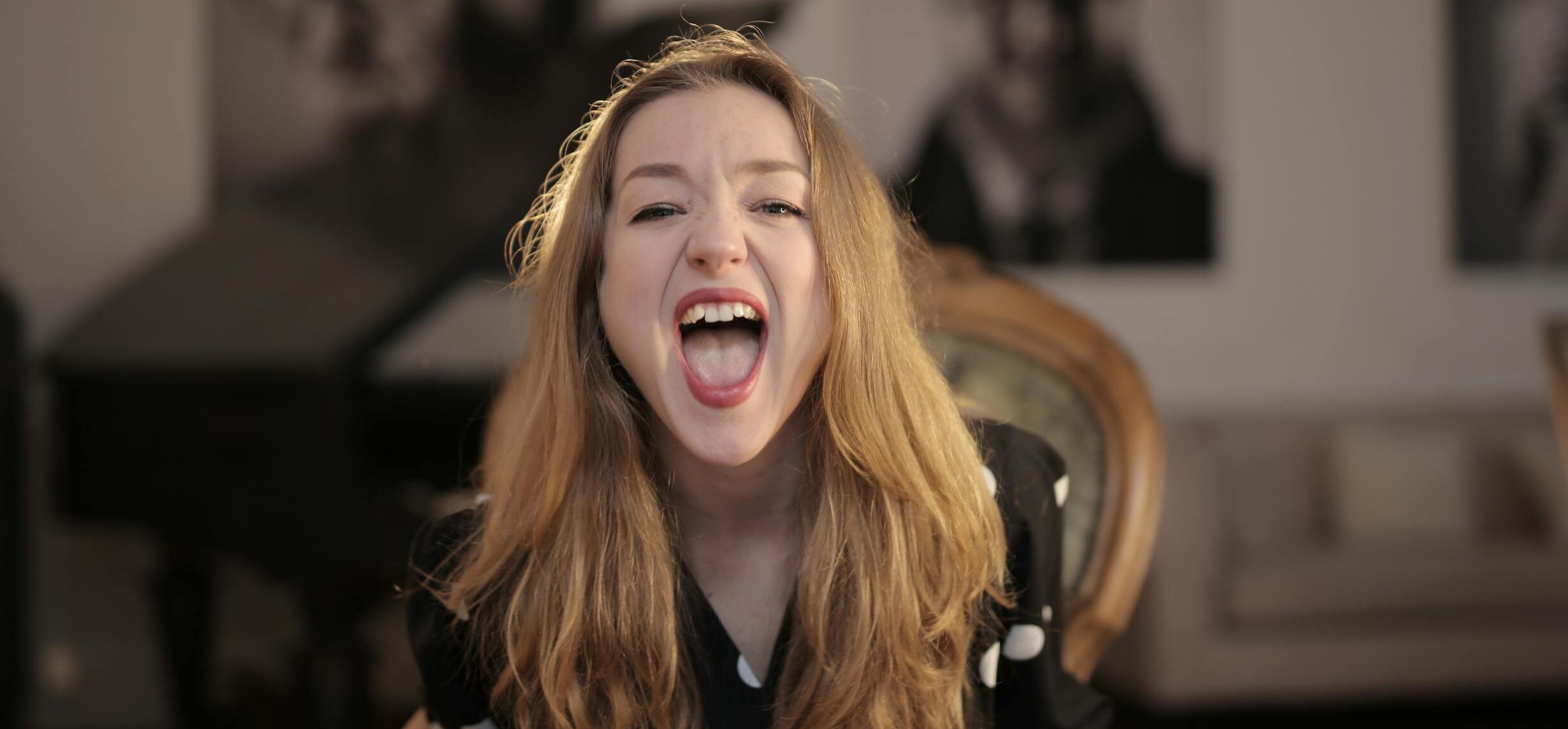 Portrait of a young woman with blonde hair expressing emotions while sitting indoors.