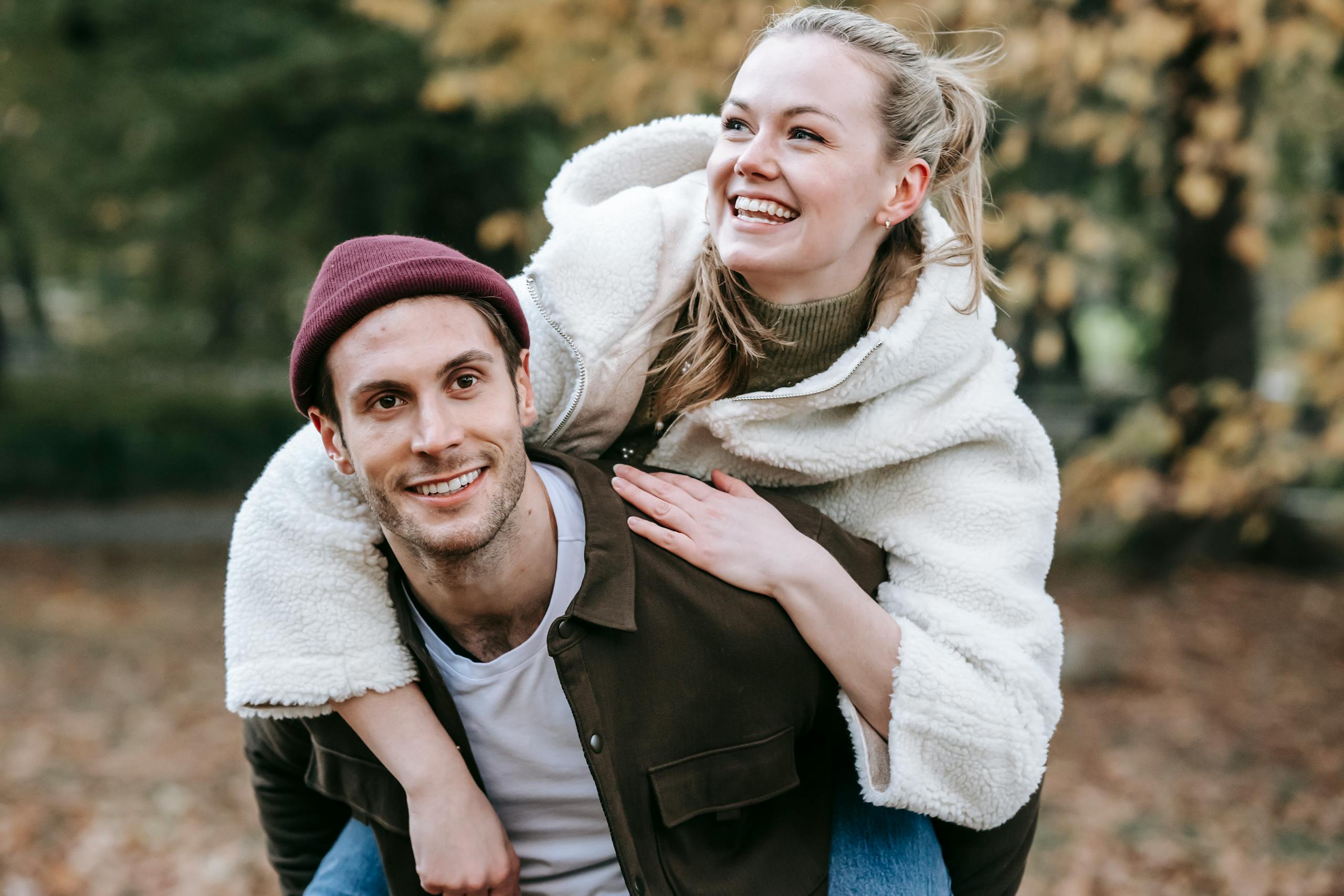 Smiling couple having fun outdoors during autumn, enjoying a playful piggyback ride.