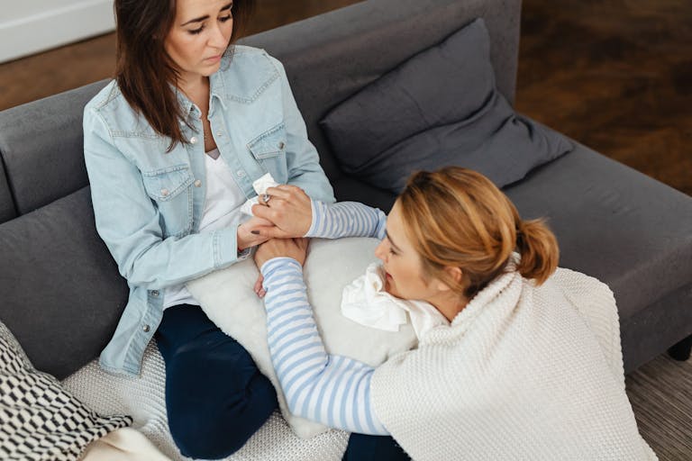 Two women showing support and comfort, sitting together indoors on a couch.