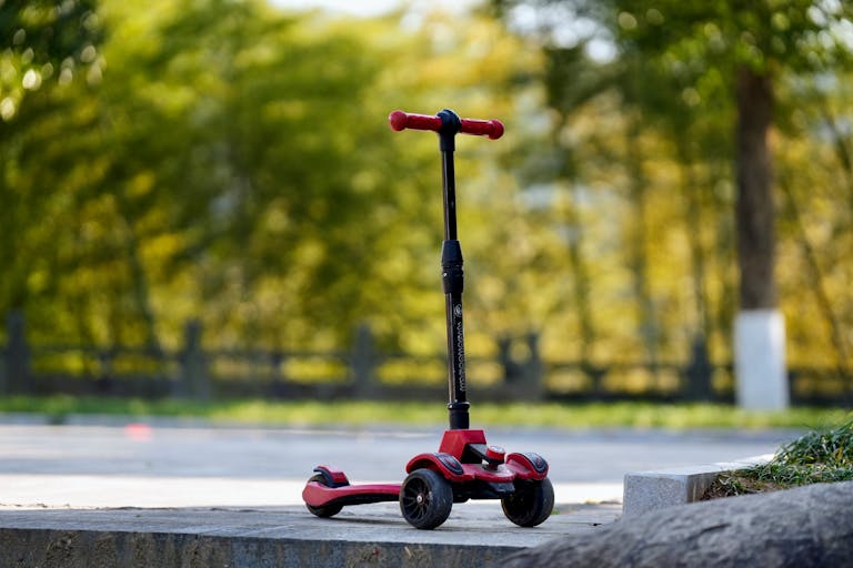 Vibrant red child's scooter in a sunny park setting, perfect for outdoor fun.