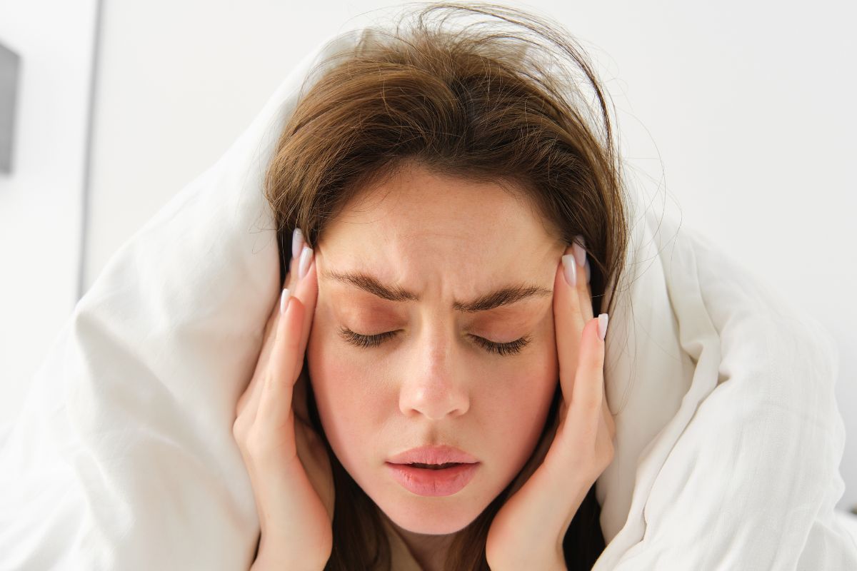 woman with a blanket over her head eyes closed hands on her temples like she's in. pain
