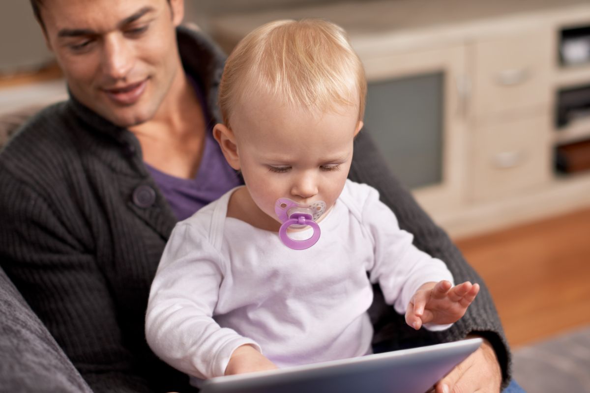 young child sitting on a mans lap with an ipad infront of him