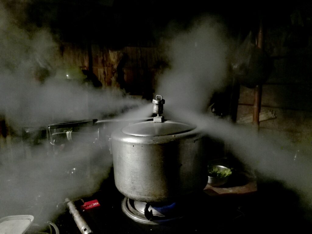 A pressure cooker releasing steam from its lid on a stove