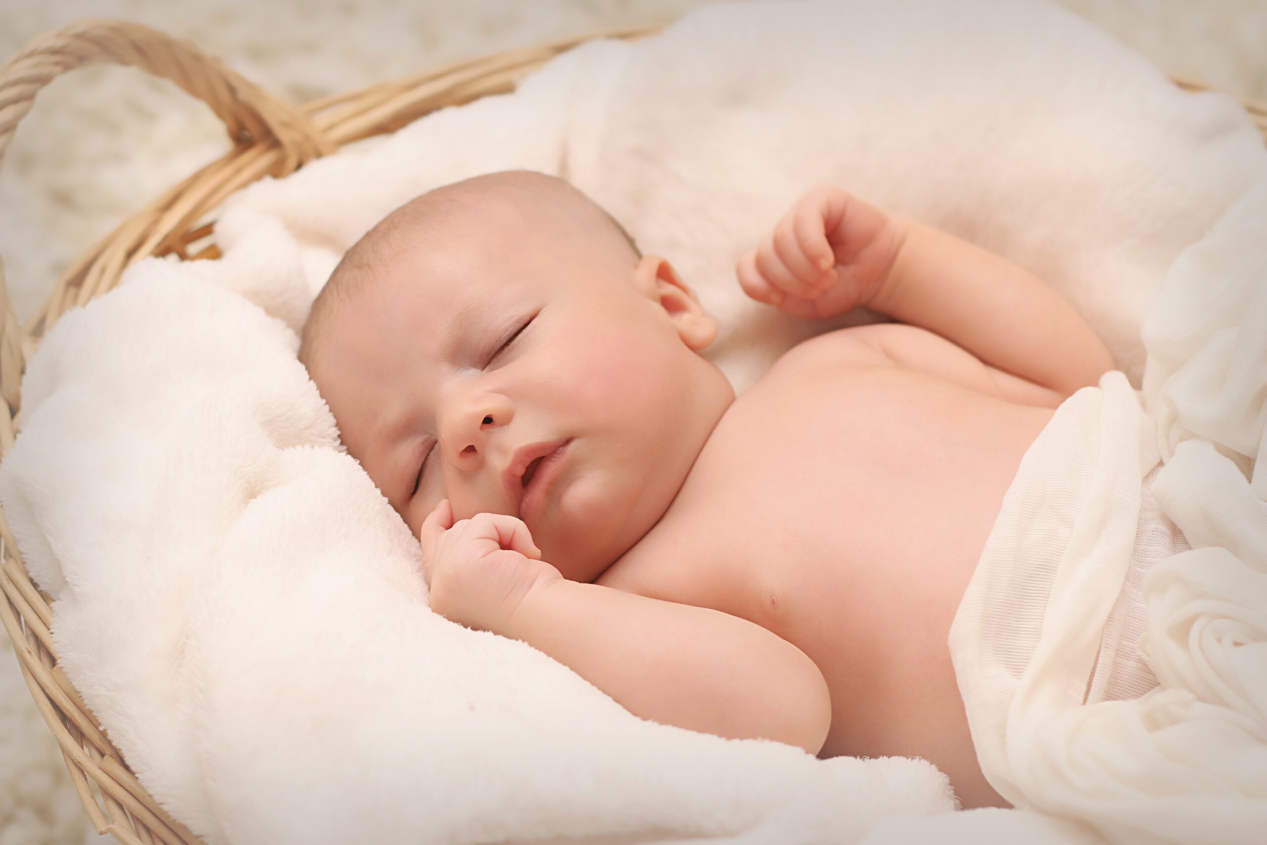 A newborn baby sleeping wrapped in a blanket inside a woven basket